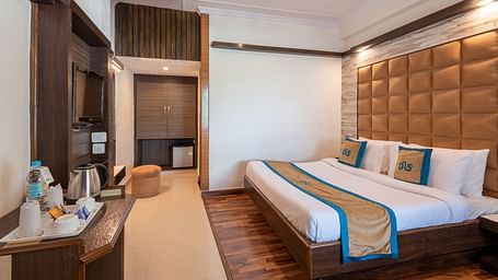 A welcoming hotel room with a comfortable bed, a TV, a mini-fridge, and a balcony offering a view - DLS Meghavan Resort